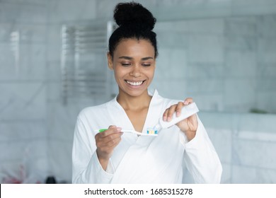 African ethnicity beautiful woman with wide healthy white perfect smile holding toothbrush with soft bristle applies toothpaste and ready to brush teeth in morning after waking up, oral care concept - Powered by Shutterstock