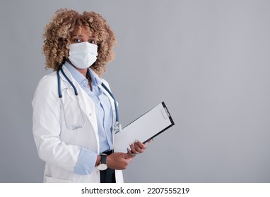 African Ethnicity Doctor Or Medical Intern With Curly Hair In A Medical Mask In A Lab Coat, Clipboard  Isolated On Grey Background  Mocap Place For Design. Health Care Concept, Medical Insurance