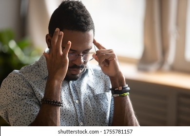 African ethnicity guy sit indoor closed eyes touches temples with fingers suffers from migraine feels unhealthy unwell. Student preparing for exams or try to remember forgotten important information - Shutterstock ID 1755781157