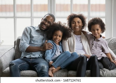 African ethnicity small siblings and parents full family portrait. Married young couple their little cute children daughter and son hugging sit on sofa in cozy light living room photo shooting at home - Powered by Shutterstock