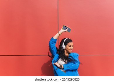 African ethnicity student happy and smiling while dancing and listening to music with energy and joy, celebrating weekend, vacation or school grades. Blue clothes and red color background wall. - Shutterstock ID 2145290825