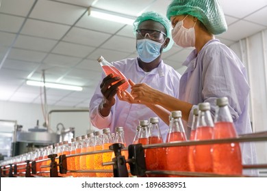 African and European specialists of beverage check quality of red juice in automatically product line of beverage industry - Shutterstock ID 1896838951