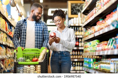 African Family Buying Food In Supermarket Shop Walking Pushing Cart And Choosing Groceries Together. Happy Customers. Black Couple In Grocery Store. Empty Space For Text - Powered by Shutterstock