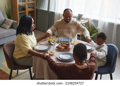 African family with children sitting at dining table with eyes closed and praying before holiday dinner at home - Powered by Shutterstock