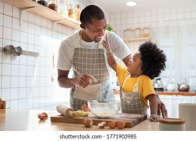 African Family Have Fun Cooking Baking Cake Or Cookie In The Kitchen Together, Happy Smiling Black Son Enjoy Playing And Touching His Father Nose With Finger And Flour While Doing Bakery At Home.