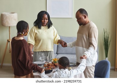 African Family Holding Hands With Children Standing Around The Dining Table In The Room And Praying