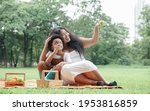 African family mother and little son sitting on mat picnic together at green park. Mom is pointing out trees for child to look at. While he enjoy eating apple