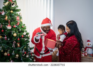 African family, Nigerian father wearing a red Santa costume open gift box for a 4-month-old son which an Asian mother holding baby, they are happy together at Christmas and New Year's Day. - Powered by Shutterstock