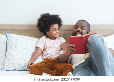 African family, single father and cute boy, lying on bed, reading a book together at home. Smiling beard dad spends time and have fun story telling with son. Happy family and education concept - Powered by Shutterstock