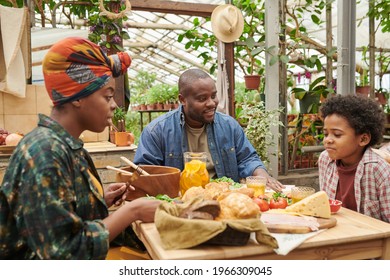 African Family Of Three Sitting At The Table With Food And Having Lunch Together In The Garden