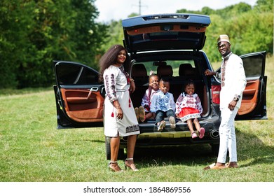 African Family In Traditional Clothes Stand Against Their Car, Kids Sit On Trunk.