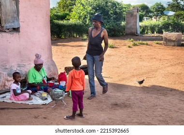 African Family In The Village, Mother Walking And Kids Sited Around Their Grandma In The Yard