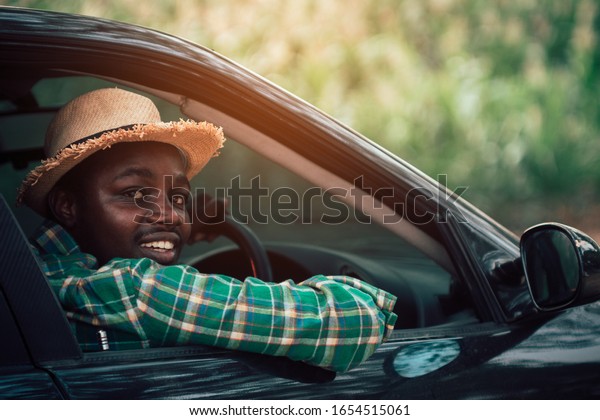 African farmer  driving and looking while sitting\
in a car with open front\
window.