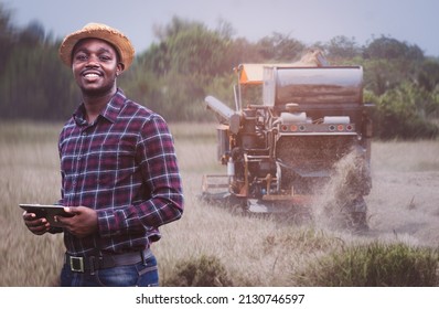 African Farmer Holding Tablet For Combine Harvester Guidance And Control On A Background Of Combine Harvester.Smart Farming Agriculture Or Cultivation Concept