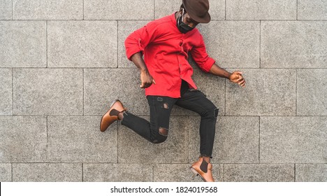 African fashion man dancing and having fun outdoor wearing protective face mask to avoid corona virus spread - Safety fun and youth millennial people lifestyle concept 