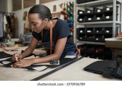 African female artisan using a pattern on leather in her shop - Powered by Shutterstock