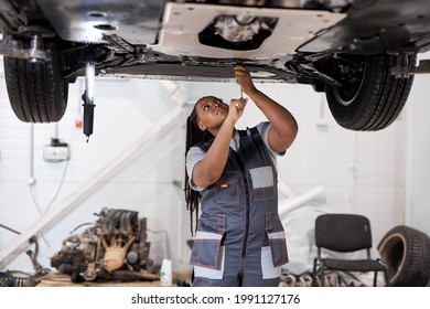 African female auto mechanic fixing car, mechanic repairing car on lift in garage. attractive confident black afro american lady in overalls concentrated on work, repair using instruments tools