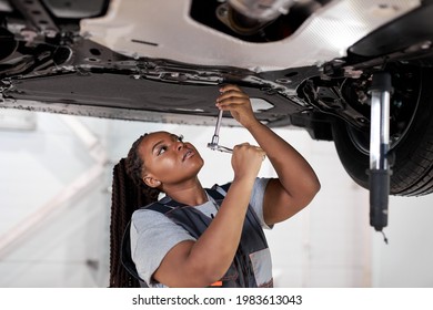 African Female Auto Mechanic Work In Garage, Car Service Technician Woman In Overalls Check And Repair Customer Car At Automobile Service Center, Inspecting Car Under Body And Suspension System