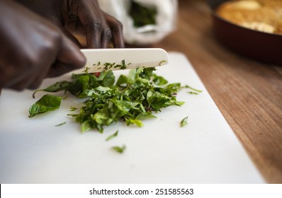 African female cook is cutting basil on a white board. In the background is an apple cake out of focus on a wooden board. - Powered by Shutterstock