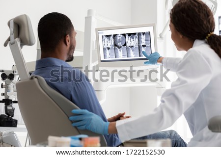 African female dentist and male patient watching xray on digital screen at modern clinic