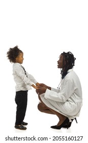 African Female Doctor Is Squatting Next To Small Boy And Talking. Side View. Full Length Studio Shot Isolated.