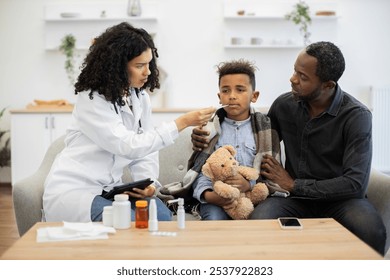 African female doctor tending to sick African boy with a thermometer at home. Concerned father supporting his son, illustrating concept of home healthcare and parental care. - Powered by Shutterstock