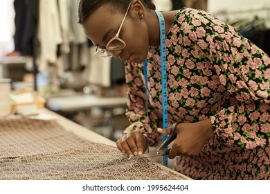 African Female Fashion Designer Cutting Cloth At A Studio Workbench