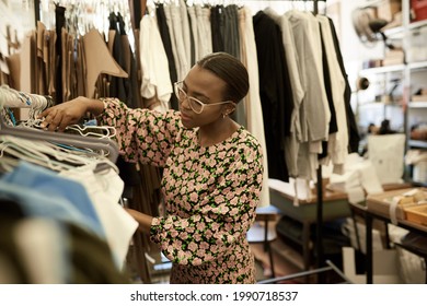 African female fashion designer looking at clothing on racks in her studio - Powered by Shutterstock