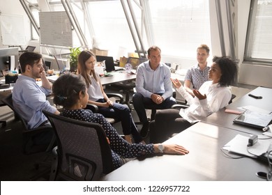 African female leader coach mentor teacher speaking to team workers interns explaining new project discussing corporate business plan at multiracial group office meeting or sales corporate training