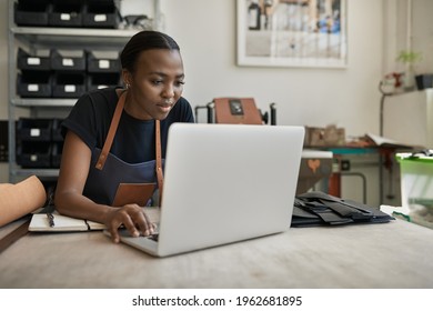 African female leather worker using a laptop at a workbench