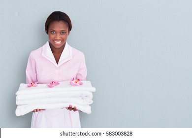 African Female Maid Holding Towels On Colored Background