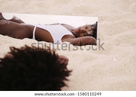 African female model lying on ocean shore looking to the mirror. Travel concept, dream of summer vacation