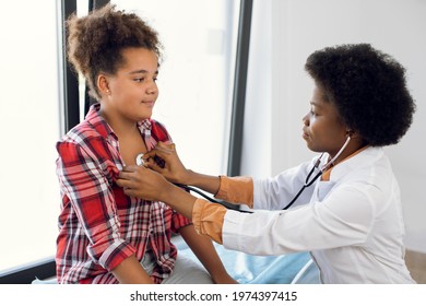 African Female Pediatrician With Stethoscope Auscultating Cute Teen Mixed Race Girl Patient. Black Physician, Checks Heartbeat And Lungs Breathing Of Kid, Making Checkup Before Vaccination