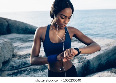 African Female Runner Checking Fitness Progress On Her Smart Watch. Woman Monitoring Workout Performance On Her Watch Outdoors.