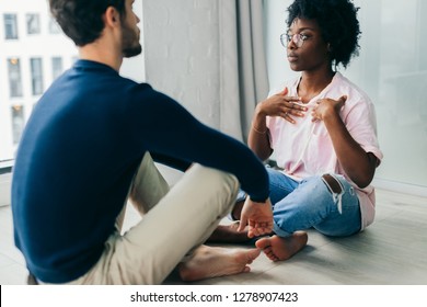 African female yoga instructor giving individual yoga class to young caucasian bearded man, staying indoors, in modern appartment.