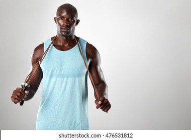 African fitness model with skipping rope against grey background. Handsome muscular man posing with jumping rope. - Powered by Shutterstock