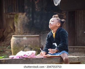 An African girl child or student sitting on a bench outside a village mud house, studying to attain excellence in her school, studies, career and education