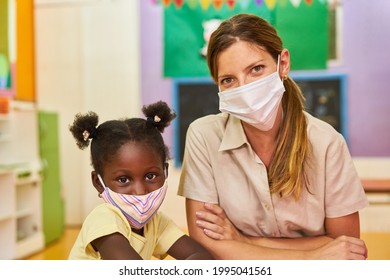 African Girl And Educator With Face Mask In Kindergarten Because Of Covid-19