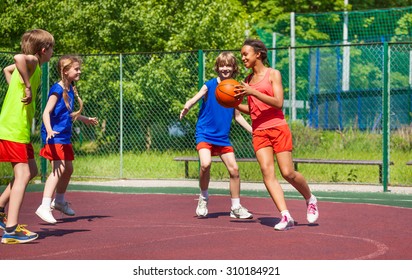 African Girl Holds Ball And Teens Play Basketball