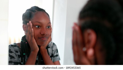 African girl looking at herself in mirror. Teenage adolescent girl standing in face reflection