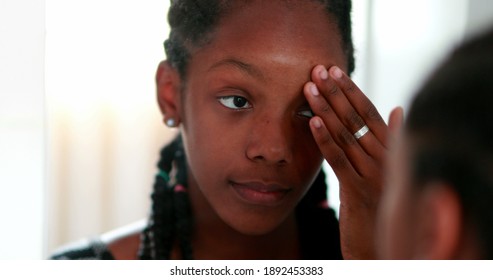 African girl looking at herself in mirror. Teenage adolescent girl standing in face reflection
