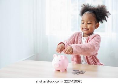 African girl looking and insert a coin into a piggybank - Shutterstock ID 2224410095