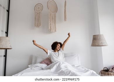 African girl in pajamas stertching in cozy bed and raising hands up at home. African american woman wake up and enjoying good morning - Powered by Shutterstock