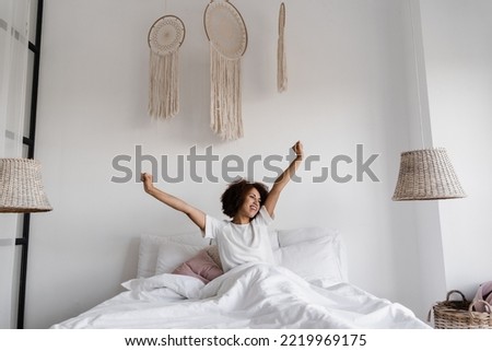 African girl in pajamas stertching in cozy bed and raising hands up at home. African american woman wake up and enjoying good morning