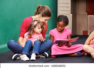 African girl reads book in kindergarten next to kindergarten teacher - Shutterstock ID 1608186052