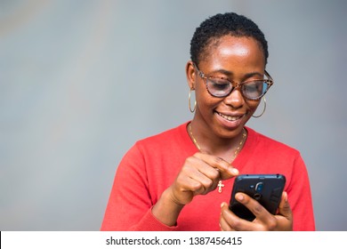 African girl with short hair and wearing glasses smiling while using her phone