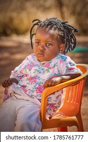 African Girl Toddler Sitting On An Orange Chair In The Yard, Village In Botswana