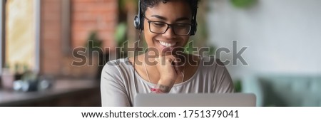 African girl wear headphones looks at pc screen watch movie, online webinar, enjoy virtual study with tutor, teacher interact with trainee via video call, horizontal banner for website header design