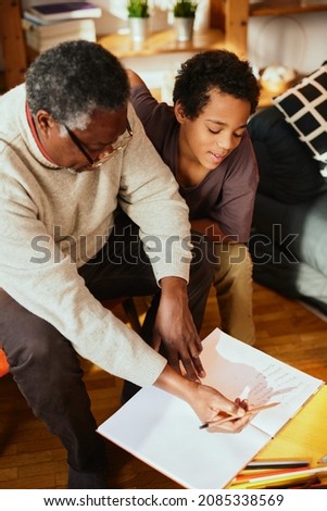 An African grandfather showing to his grandson how to solve a math problem. Family support