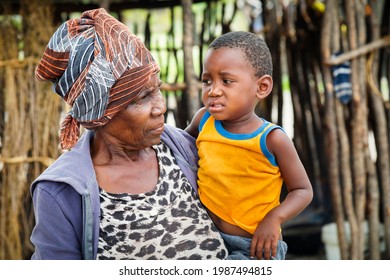 African Granny Holding Her Grandson In Front Of Her Shack Village In Botswana